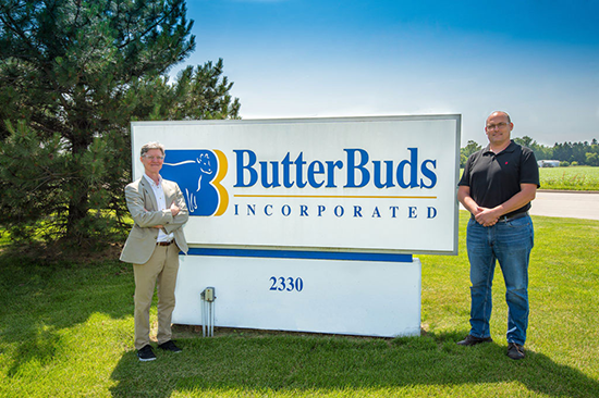 two guys standing next to butterbuds sign